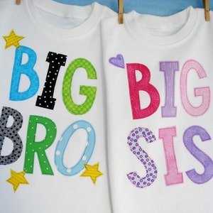 May include: Two white t-shirts with the words "BIG BRO" and "BIG SIS" in colorful fabric letters. The letters are decorated with stars and hearts.