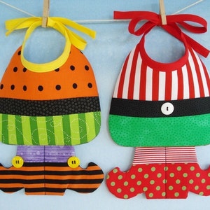 May include: Two handmade fabric bibs with a whimsical elf and witch design. The elf bib is red and white striped with a green and white polka dot bottom and the witch bib is orange with black polka dots and green and black stripes.