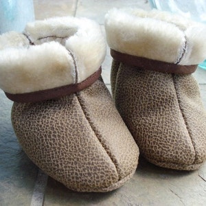 May include: A pair of brown leather baby booties with a faux fur trim. The booties have a textured leather exterior and a soft, plush lining.