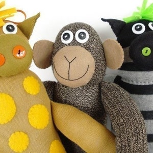 May include: Three sock puppets, a giraffe, a monkey, and a zebra, are made from colorful socks and fabric scraps. The giraffe is brown with yellow spots, the monkey is brown with black eyes, and the zebra is black and white with green eyes.