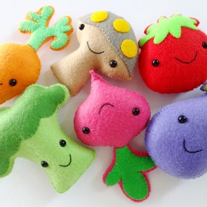 Puede incluir: Un conjunto de siete juguetes de peluche de fieltro con forma de verduras y un hongo. Los juguetes tienen caras sonrientes y son de varios colores, incluyendo verde, naranja, rojo, morado, rosa y marrón.