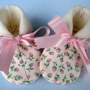 May include: A pair of baby booties with a pink floral print and pink satin ribbon bows. The booties have a white fleece lining.