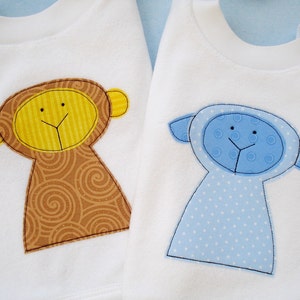 May include: Two white baby onesies with embroidered animal appliques. One onesie features a brown monkey with yellow face and swirl pattern. The other onesie features a blue lamb with white polka dots.