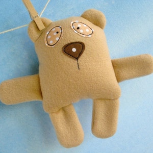 May include: A brown plush teddy bear with white and brown eyes and a brown nose. The bear is hanging from a clothesline.