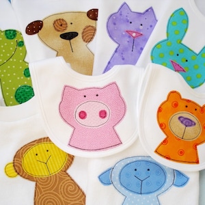 May include: A set of six baby bibs with embroidered animal designs. The bibs are white with a variety of colorful animals, including a frog, a dog, a cat, a pig, a bunny, and a monkey.