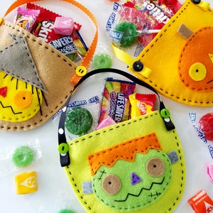 May include: Three felt Halloween trick-or-treat bags with different character designs. The bags are yellow, orange, and green with stitched details. The bags are filled with sweets and lollipops.
