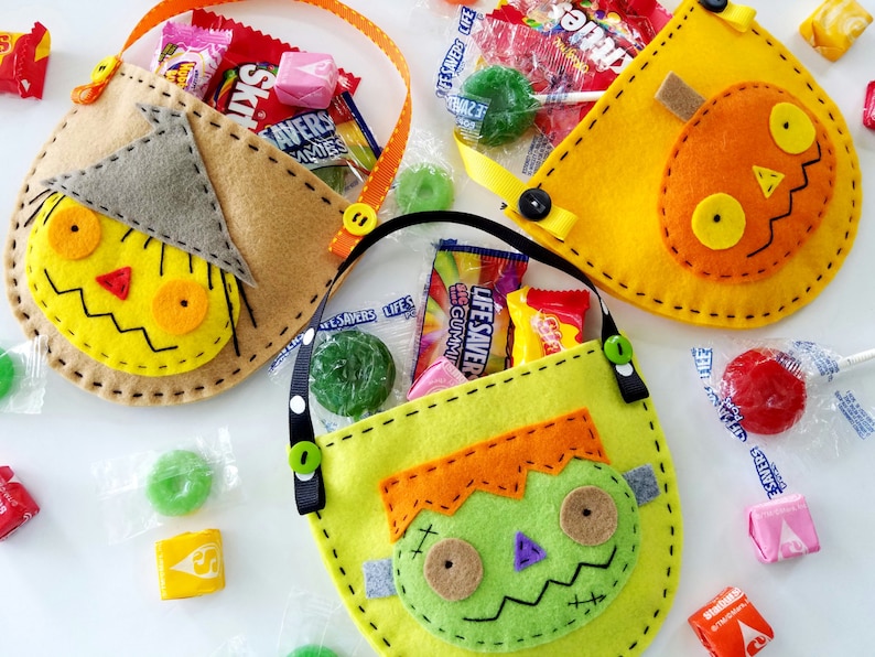 May include: Three felt Halloween trick-or-treat bags with different character designs. The bags are yellow, orange, and green with stitched details. The bags are filled with sweets and lollipops.