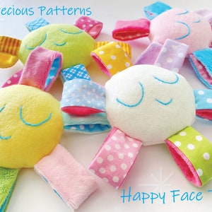 May include: Four colorful plush toys shaped like suns with smiling faces and embroidered eyes. Each toy has six fabric arms with different patterns, including polka dots, stripes, and checkered designs. The toys are arranged on a white surface.  Happy Face Toy.