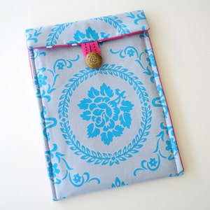 May include: A gray and blue patterned fabric iPad case with a pink fabric trim and a gold button closure.