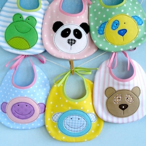 May include: A collection of baby bibs in various colors and patterns. Each bib features an animal face, including a frog, panda, dog, monkey, and bear. The bibs are made of soft fabric and have a neck tie. The bibs are hanging on a clothesline.