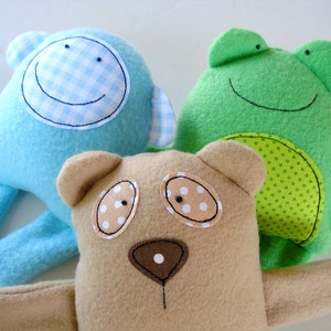 May include: Three plush toys: a blue monkey with a gingham smile, a green frog with a dotted belly, and a brown bear with polka dot eyes.