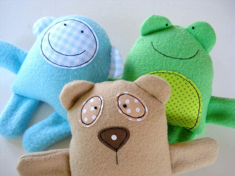May include: Three plush toys: a blue monkey with a gingham smile, a green frog with a dotted belly, and a brown bear with polka dot eyes.