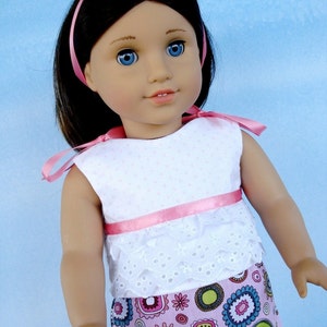 May include: A doll with long brown hair wearing a white and pink dress with a pink ribbon headband and a colorful floral print skirt.