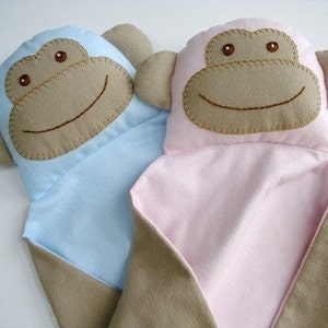 May include: Two plush monkey baby blankets, one blue and one pink. Each blanket features a brown felt monkey face with embroidered eyes and a smile.
