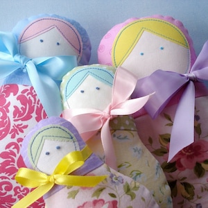 May include: Four handmade fabric dolls with embroidered faces and colourful ribbon bows. Each doll is dressed in a different patterned fabric, including pink floral, white and pink damask, and yellow and white polka dot.