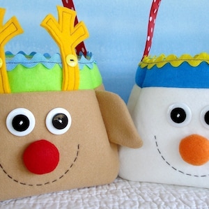 Puede incluir: Dos bolsas de regalo de Navidad de fieltro, una con forma de reno con piel marrón, cuernos amarillos y ojos saltones, y la otra con forma de muñeco de nieve con piel blanca, ojos negros y una nariz naranja.