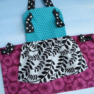 May include: A turquoise and white polka dot fabric apron with black ribbon ties and a black and white leaf print ruffle. The apron has a pink and white floral print bottom.