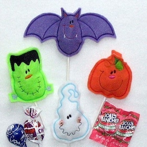 May include: A collection of Halloween-themed felt decorations, including a purple bat, a green Frankenstein's monster, an orange pumpkin, and a white ghost. Also includes wrapped lollipops and Jolly Rancher watermelon candies.
