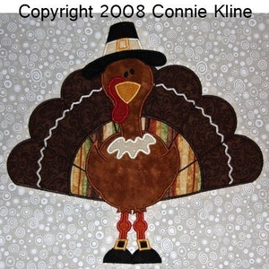 May include: A brown and white turkey wearing a black pilgrim hat with a gold buckle. The turkey has a red wattle and a yellow beak. The turkey's tail feathers are brown and white with a paisley pattern. The turkey is standing on a grey background with white circles.