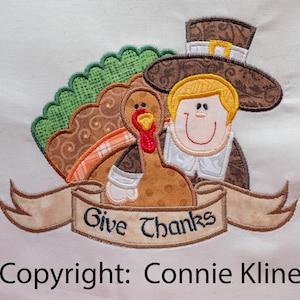 May include: Embroidered design featuring a pilgrim with a brown hat and a turkey. The design includes a banner with the text "Give Thanks".
