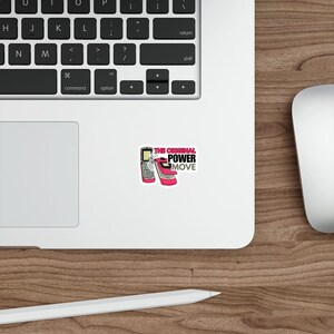 May include: A white sticker featuring a retro flip phone and a pink high-heeled shoe. The sticker has the text "THE ORIGINAL POWER MOVE" in pink and black. The sticker is on a white surface, near a laptop keyboard and a mouse.