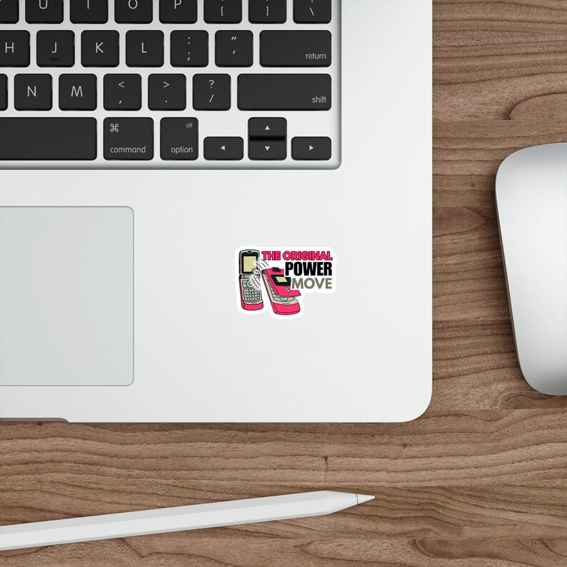 May include: A white sticker featuring a retro flip phone and a pink high-heeled shoe. The sticker has the text "THE ORIGINAL POWER MOVE" in pink and black. The sticker is on a white surface, near a laptop keyboard and a mouse.