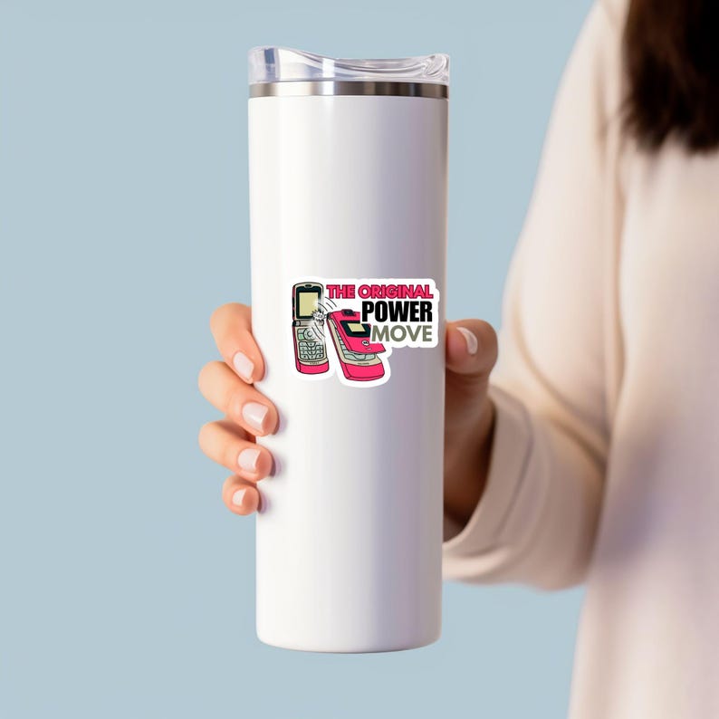 May include: A white insulated tumbler with a sticker featuring two retro cell phones and the text "THE ORIGINAL POWER MOVE" in pink and black. The tumbler is held by a person.