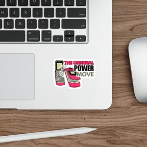 May include: A sticker featuring two pink flip phones with the text "THE ORIGINAL POWER MOVE" in black and gray. The sticker is placed on a white surface next to a laptop keyboard and a computer mouse.