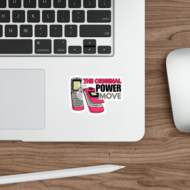 May include: A sticker featuring two pink flip phones with the text "THE ORIGINAL POWER MOVE" in black and gray. The sticker is placed on a white surface next to a laptop keyboard and a computer mouse.