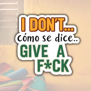 May include: A sticker with the text "I DON'T... cómo se dice... GIVE A F*CK" in orange, black, and green. The sticker has a white border and is set against a light brown background. A colorful blanket is visible in the lower left corner.