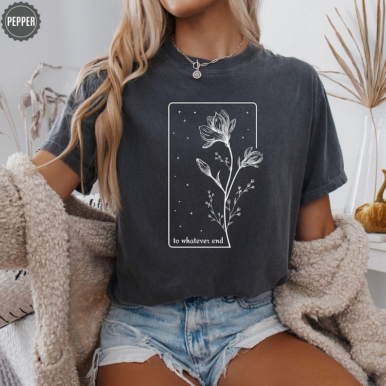May include: A dark gray t-shirt with a white graphic of a flower with the text "to whatever end" printed on the front.