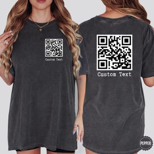 May include: Two black t-shirts with a white QR code and the text "Custom Text" printed on them.