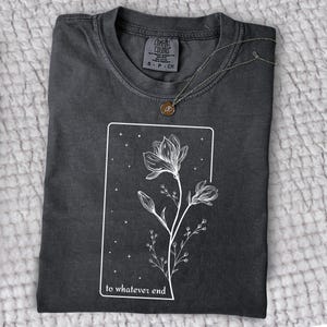 May include: A dark gray t-shirt with a white graphic of a flower with the text "to whatever end" printed on the front.