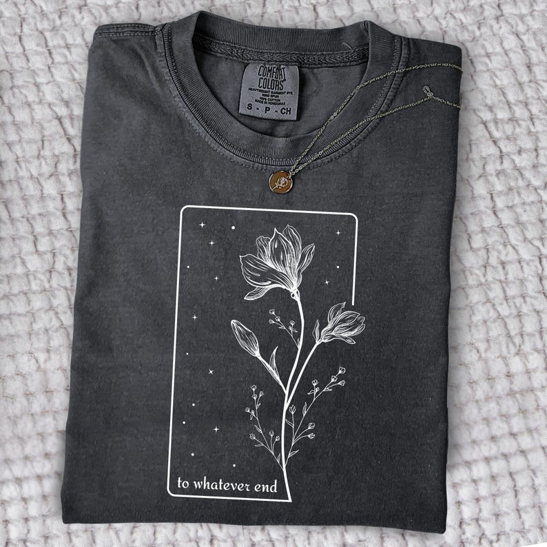 May include: A dark gray t-shirt with a white graphic of a flower with the text "to whatever end" printed on the front.