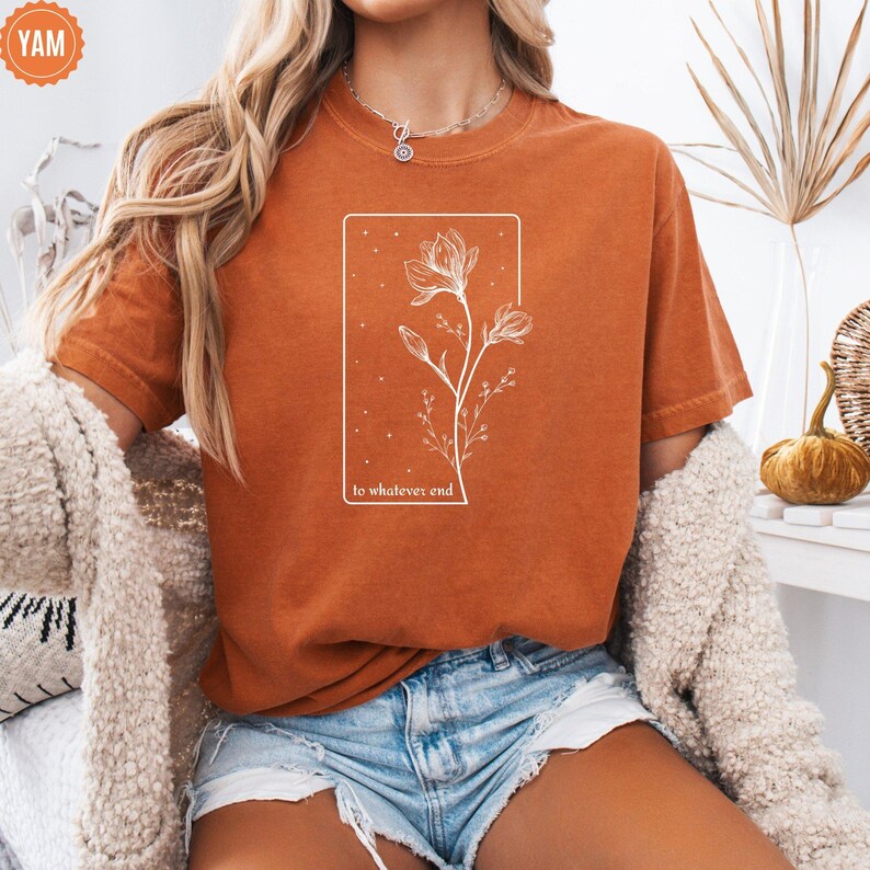 May include: A burnt orange t-shirt with a white floral design and the text "to whatever end" printed on the front.