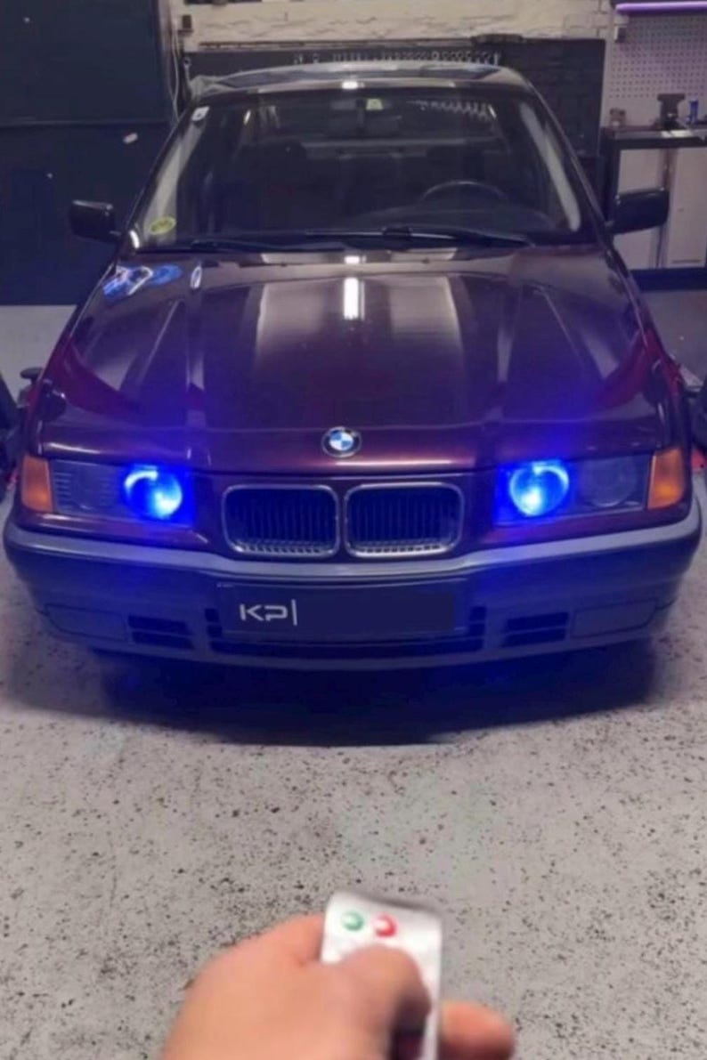 Op de afbeelding: Een donkerpaarse BMW met blauwe LED-koplampen en een "KPI" kentekenplaat. Een hand houdt een afstandsbediening met groene en rode knoppen.