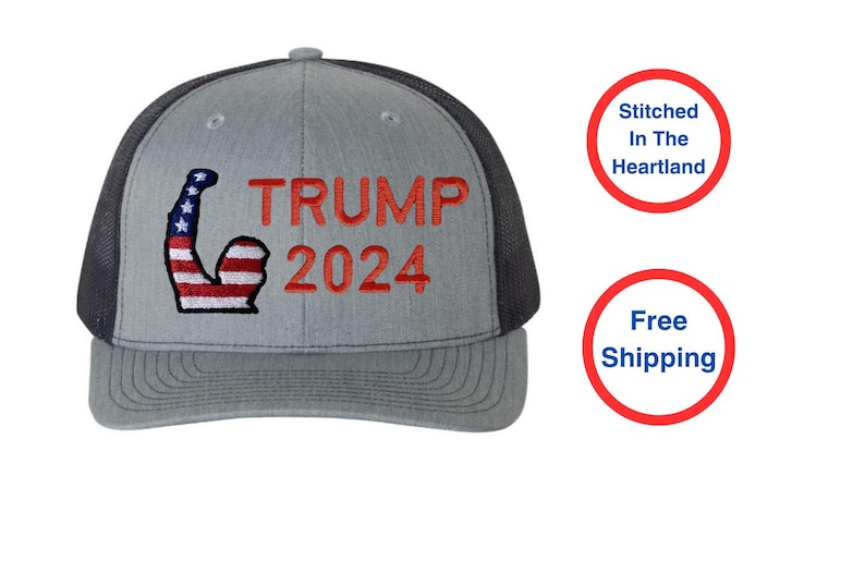 May include: Gray trucker hat with a black mesh back and a curved brim. The front features the text "TRUMP 2024" in red, with a flexed arm graphic in red, white, and blue.