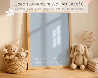 May include: A framed blue print with the text "my heart sails wherever you are" sits on a wooden surface. A woven basket with two stuffed animals and a knitted bunny are on the left. A knitted bunny and a stack of folded towels are on the right. The text "Ocean Adventure Wall Art Set of 8" is at the top.