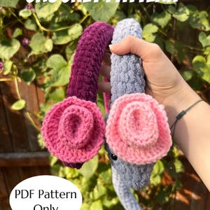 May include: Crochet pattern for a plush toy, featuring a dark purple and a grey plush with pink crochet flowers. The text "CROCHET PATTERN" is at the top, and "PDF Pattern Only" is at the bottom. Made by @GetHookedbyJules.