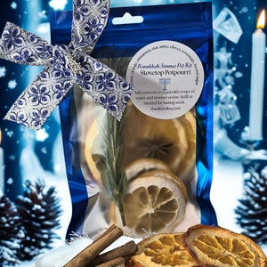 May include: A blue cellophane bag tied with a silver and blue bow, containing dried orange slices, cinnamon sticks, and rosemary. The bag has a label that reads "Hanukkah Simmer Pot Kit Stovetop Potpourri."