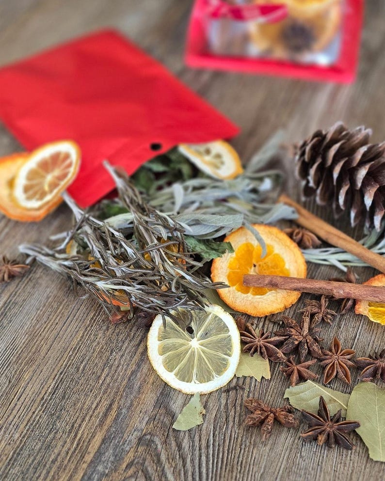 Rosemary, dried oranges, cinnamon sticks from simmer pot contents spread out from a red bag with a pinecone on the side.