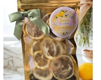 May include: A gold-colored, sealed bag filled with dried lemon slices, tied with a sage green ribbon. A circular label reads "Lemon Bloom" with floral illustrations. The bag contains a handcrafted shower kit.