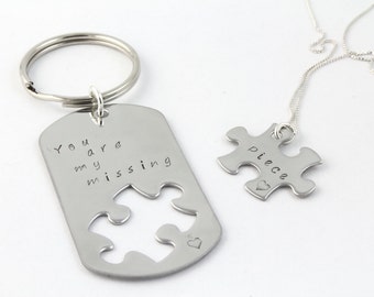 May include: A silver keychain with a puzzle piece cutout and the text "You are my missing piece" and a silver necklace with a puzzle piece pendant that says "piece" with a small heart.