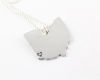 May include: Silver necklace featuring a pendant shaped like the state of Ohio with a small heart cutout.