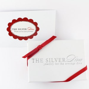 May include: A white gift box with a red ribbon and the text "THE SILVER Diva jewelry for the average diva". The box is sitting on a white surface.