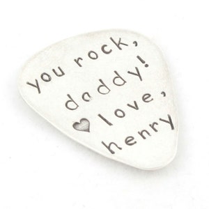 May include: Silver guitar pick with the text "You rock, daddy! Love, Henry" engraved on it.