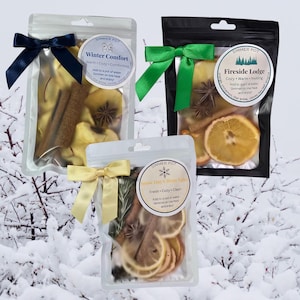 May include: Three simmer pot sachets with dried fruit, spices, and ribbons. The sachets are labeled "Winter Comfort", "Fireside Lodge", and "Snow Day Citrus Spice". Each sachet contains a mix of dried fruit, cinnamon sticks, and star anise.