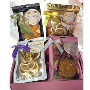Puede incluir: Cuatro bolsas selladas de rodajas de cítricos secos y botánicos, cada una atada con una cinta. Las bolsas son negras, doradas, transparentes y rosas. Las bolsas tienen etiquetas con textos como "Mom's Kitchen", "You Are My Sunshine", "Thank You, Mom" y "Love You Mom".