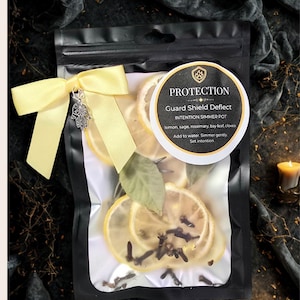 May include: A black package tied with a yellow ribbon and a silver hand charm. The package contains dried lemon slices, cloves, and bay leaves. A circular label reads "PROTECTION Guard Shield Deflect INTENTION SIMMER POT".