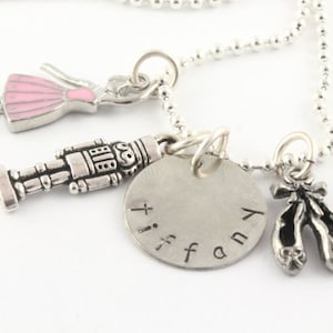 May include: Silver necklace with multiple charms, including a ballerina, a nutcracker, a silver disc with the name "Tiffany" engraved on it, and a pair of ballet shoes.